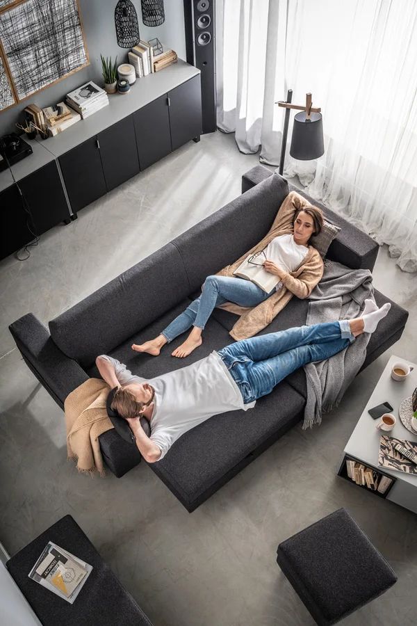 Ciemnoszara sofa z funkcją spania, na której relaksuje się para.